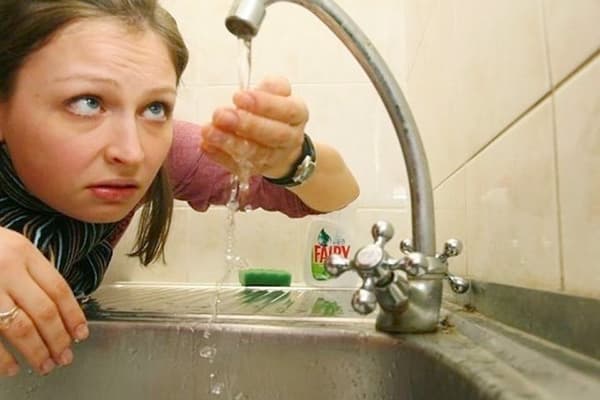 Moteris žiūri į vandenį iš čiaupo