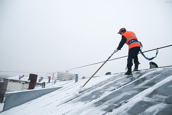 Būsto ir komunalinių paslaugų darbuotojas valo siūlės stogą nuo sniego