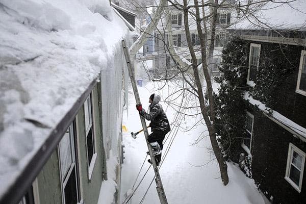 Vyras kopėčiomis lipa ant sniego stogo